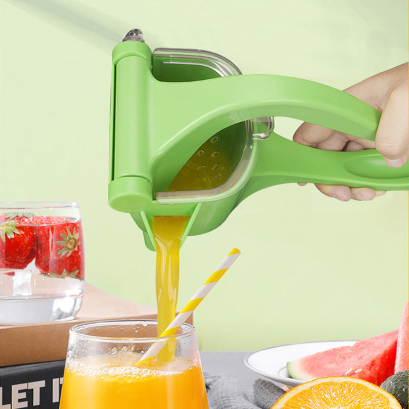 Green manual juicer squeezing orange juice with a glass of juice and fruits in the background.