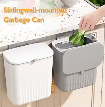 Sliding wall-mounted garbage can with a hand placing green leaves into it, set against a kitchen counter.